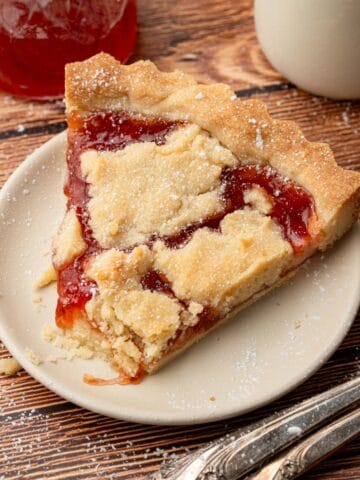 A piece of the strawberry jam tart on a plate with powdered sugar on top.