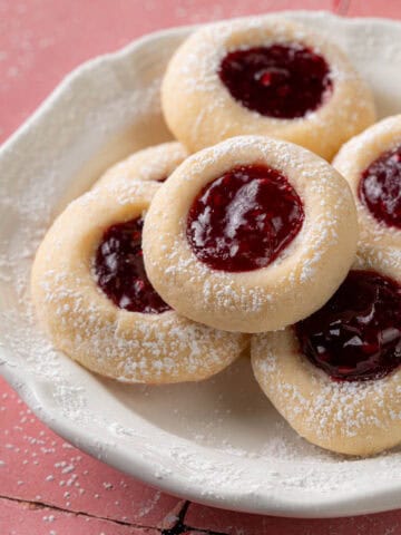 Thumbprint cookies with raspberry in the middle on a plate.