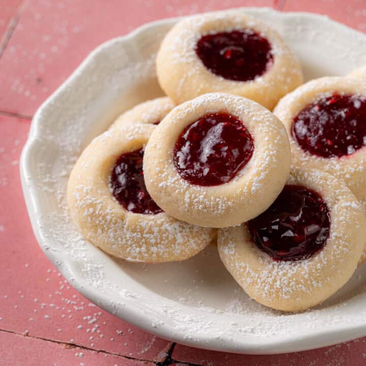 Thumbprint cookies with raspberry in the middle on a plate.