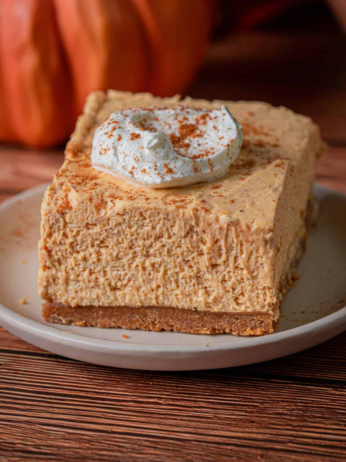 A slice of the pumpkin cheesecake on a plate with whipped cream.