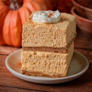 A stack of no bake pumpkin cheesecake bars with whipped cream and cinnamon on top.
