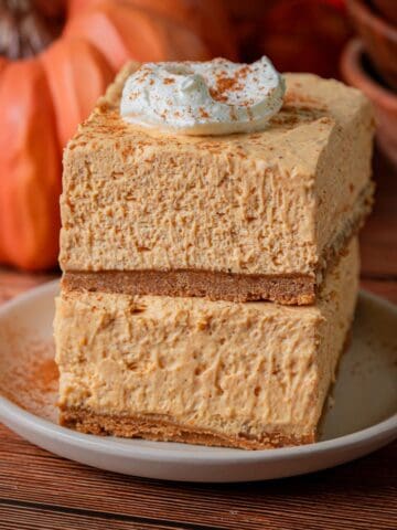 A stack of no bake pumpkin cheesecake bars with whipped cream and cinnamon on top.