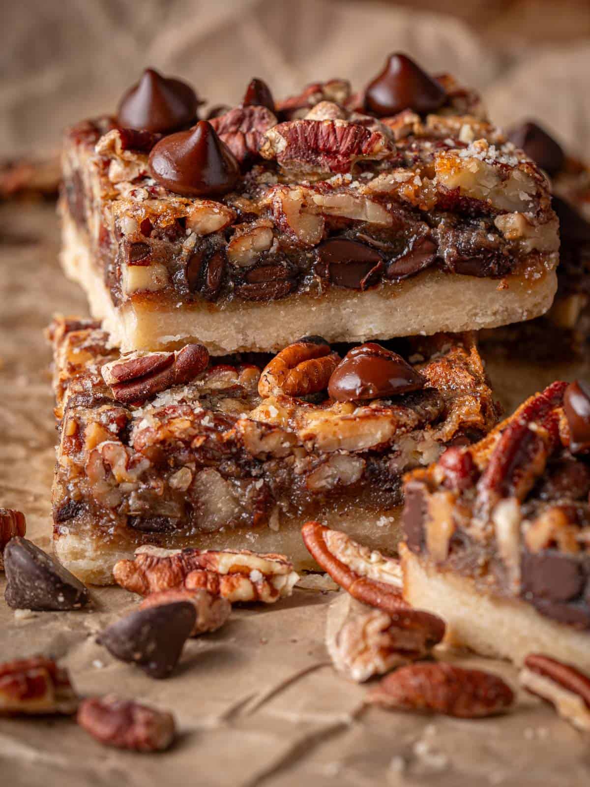 A stack of the bars on top of each other with pecans and chocolate around.