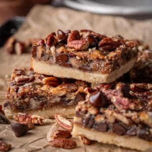Pecan bars with chocolate chips and pecans all around on parchment paper.