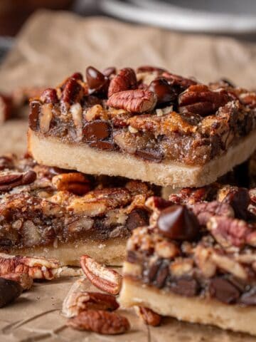 Pecan bars with chocolate chips and pecans all around on parchment paper.