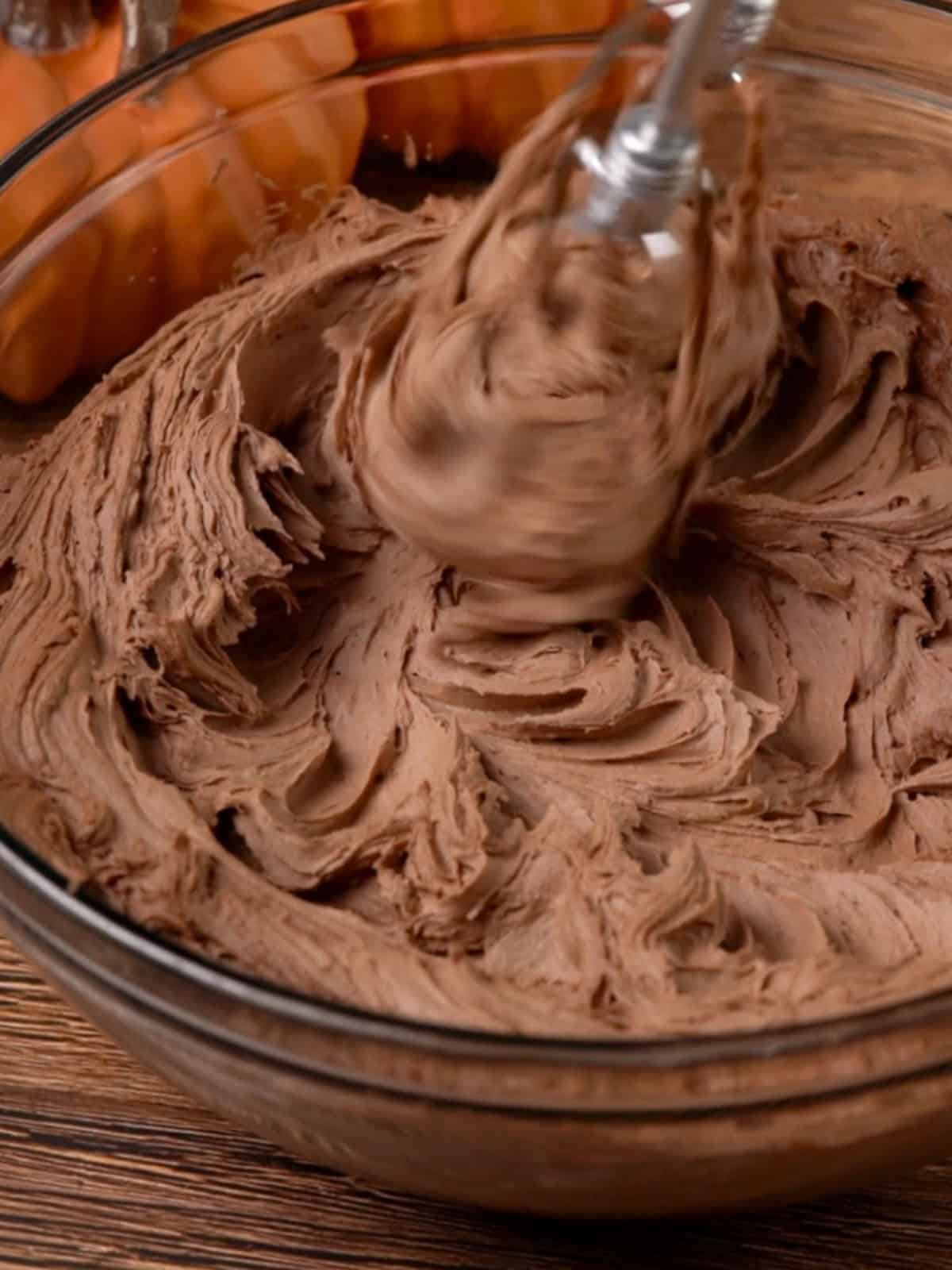 Chocolate frosting in a bowl being mixed until fluffy and combined.