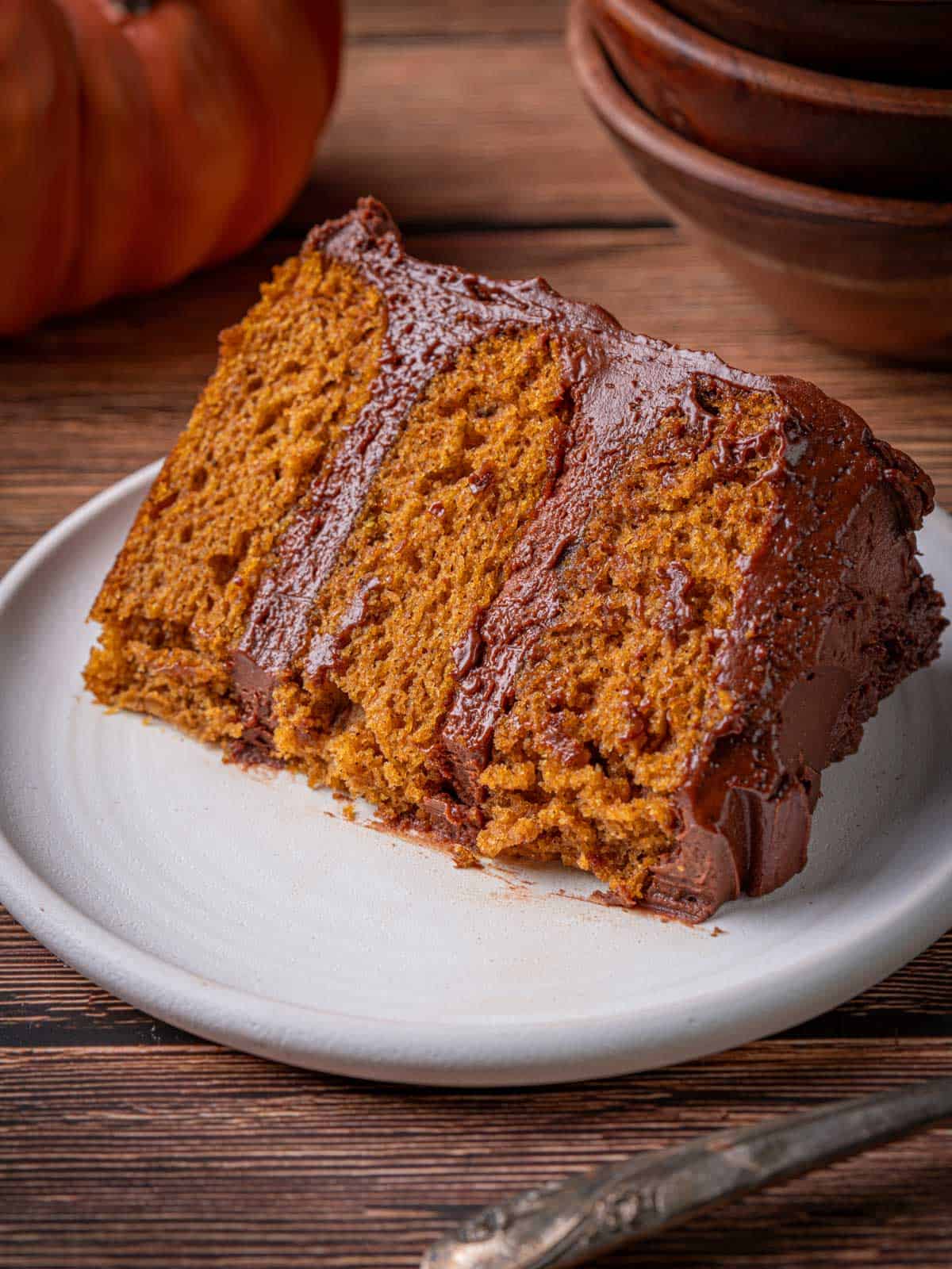 A slice of cake showing the layers on a plate with pumpkin in the background.