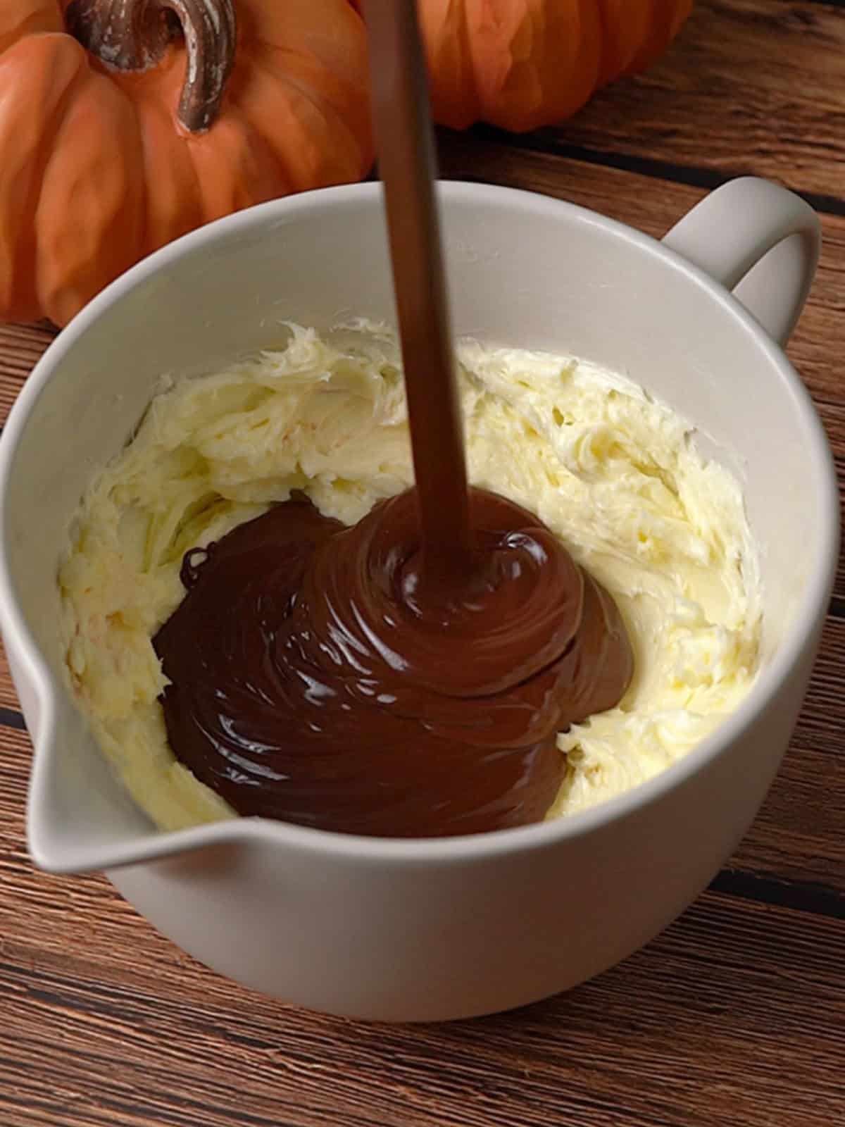 Melted chocolate being added to butter in a bowl on the counter.