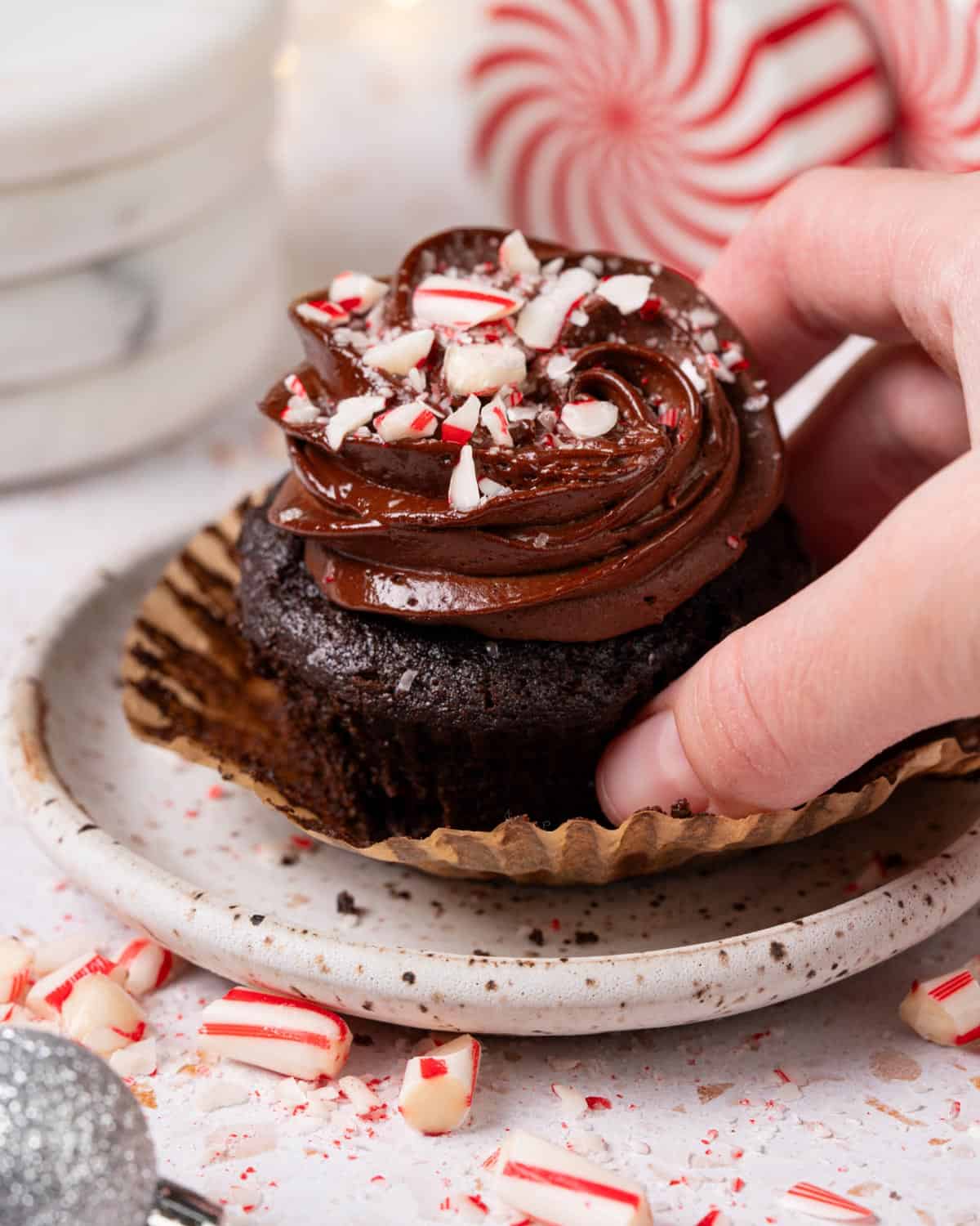 A chocolate cupcake with chocolate ganache on top with peppermint candies.