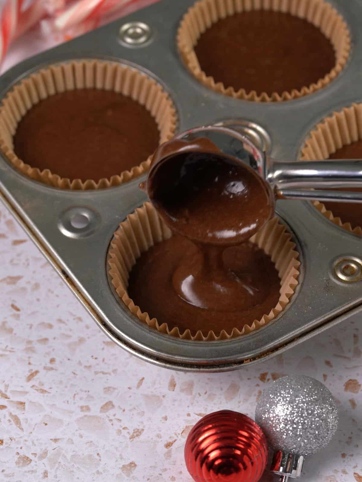 Chocolate cake batter being poured into cupcake liners.
