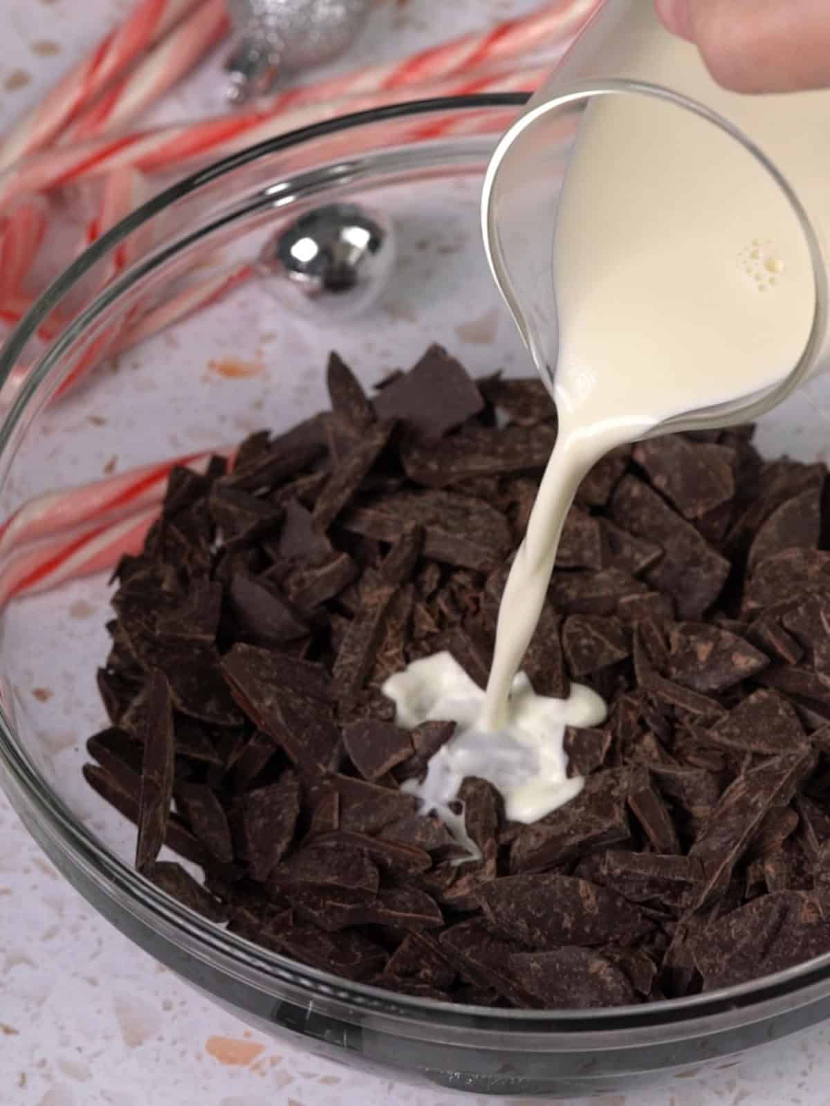 Heavy cream being poured over chopped chocolate in a bowl.