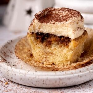 Tiramisu cupcake on a white plate with cocoa powder around.