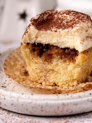 Tiramisu cupcake on a white plate with cocoa powder around.