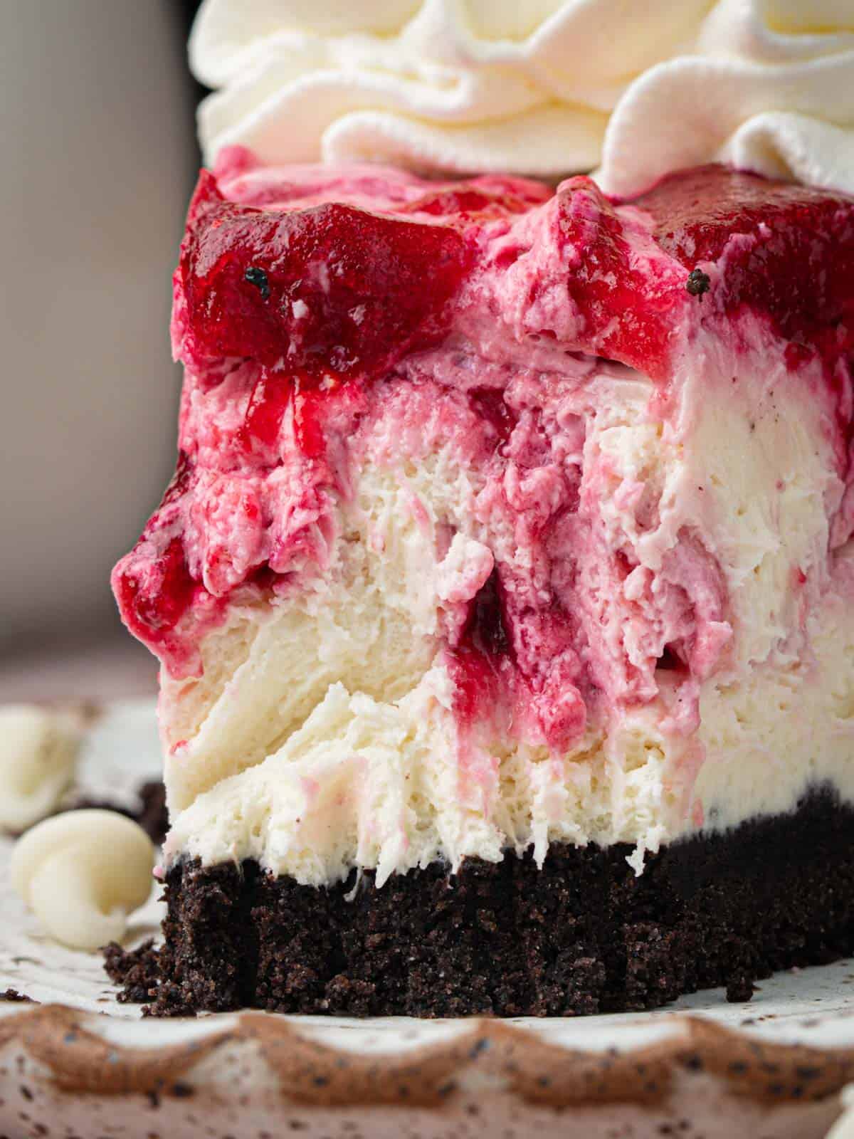 White chocolate cranberry cheesecake on a plate with whipped cream.