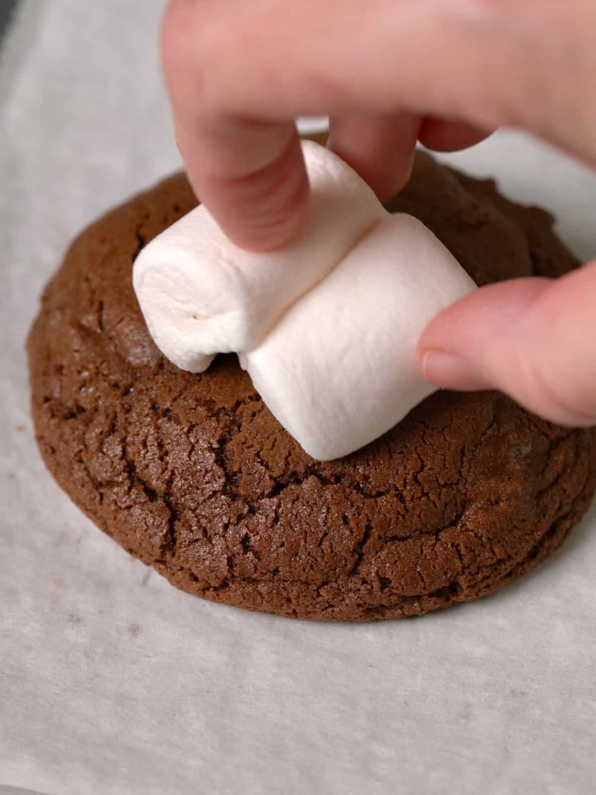 Placing a marshmallow on top of the baked cookie on parchment paper.