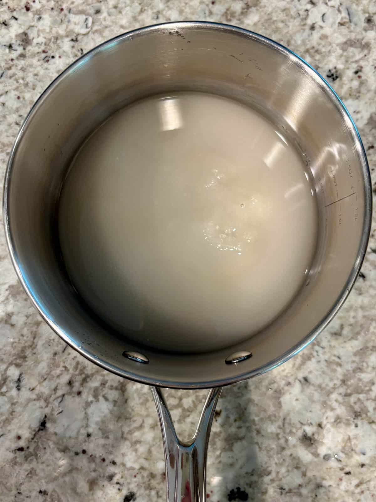 Granulated sugar and water in a saucepan on the counter.