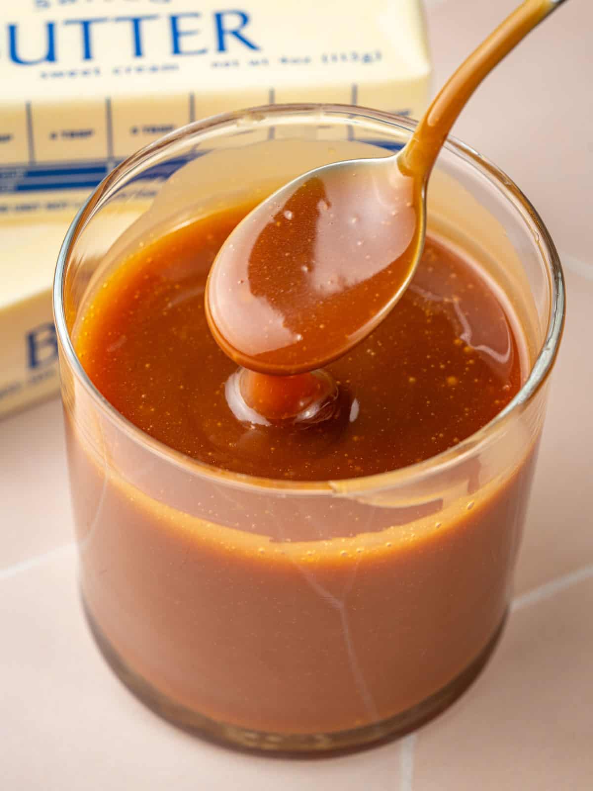 A spoon with caramel on it in a jar with butter in the background.