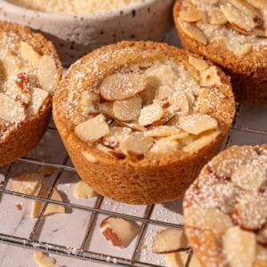 Almond cookie cups on a rack with sliced almonds and powdered sugar.