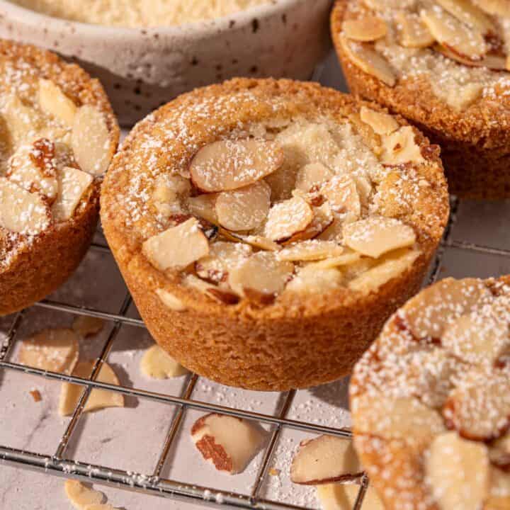 Almond cookie cups on a rack with sliced almonds and powdered sugar.