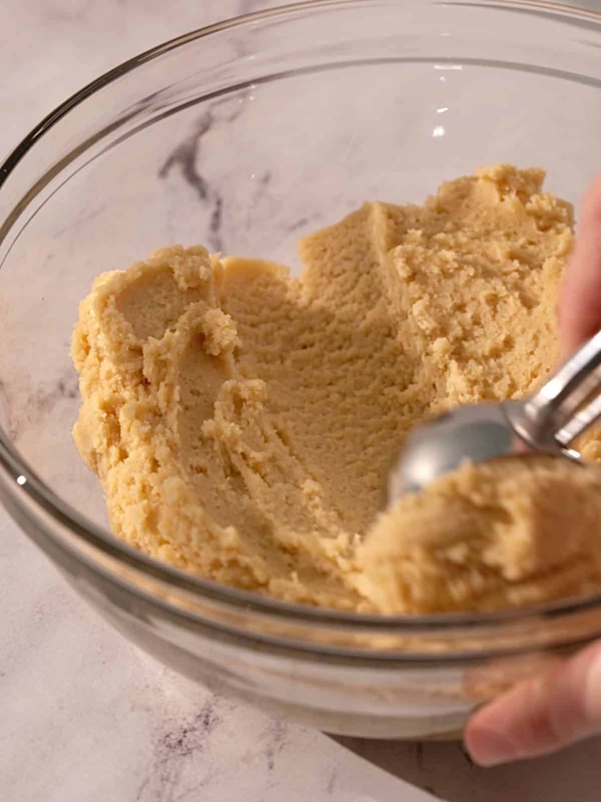 Almond sugar cookie dough in a bowl being scooped out.