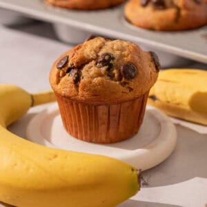 Chocolate chip banana muffin with bananas around and a muffin pan.