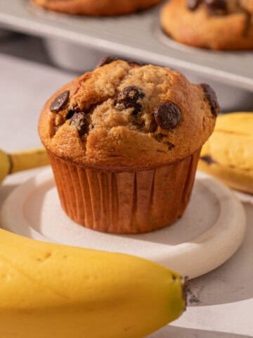 Chocolate chip banana muffin with bananas around and a muffin pan.