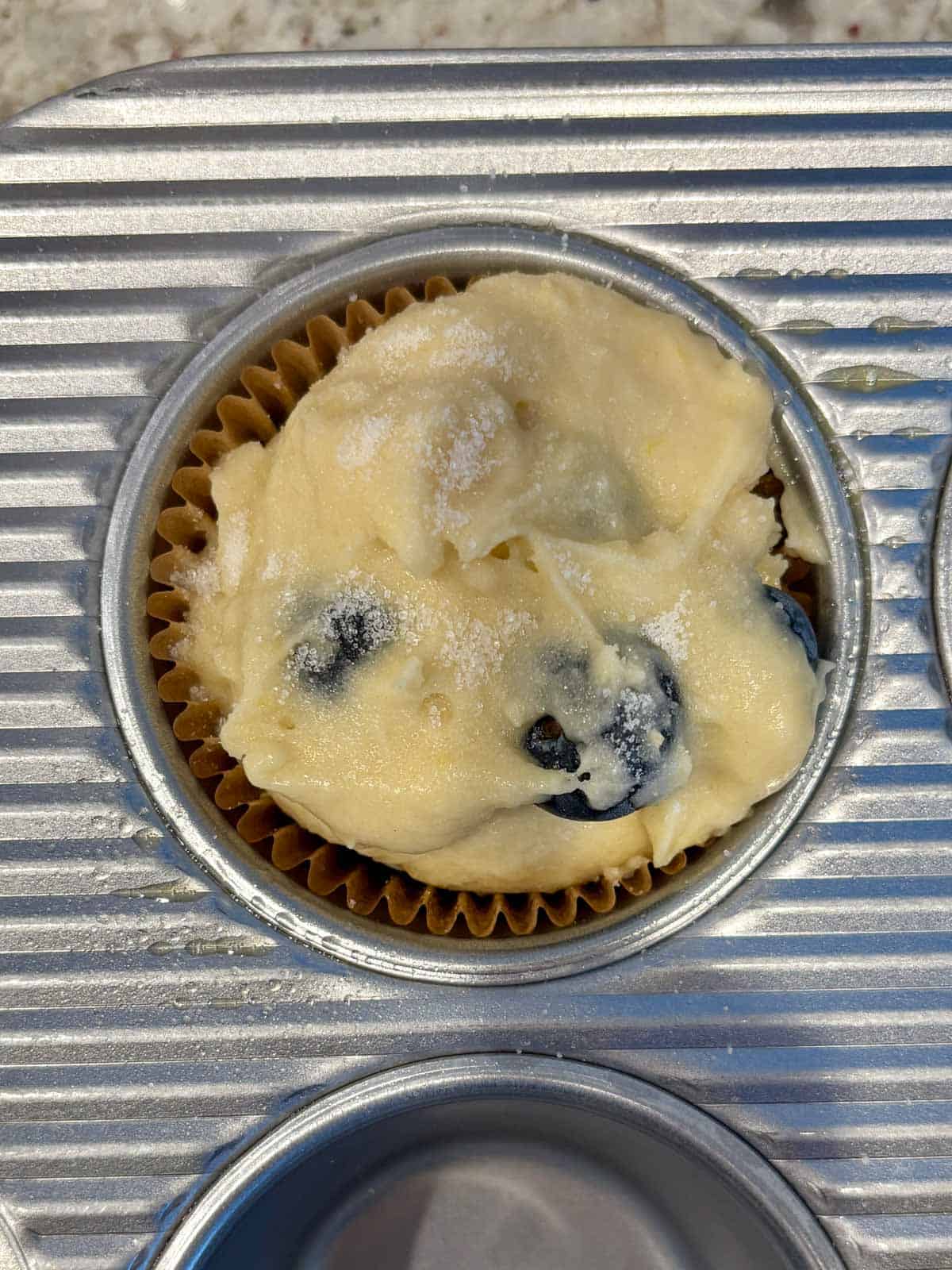 Muffin batter in a muffin pan with granulated sugar on top.