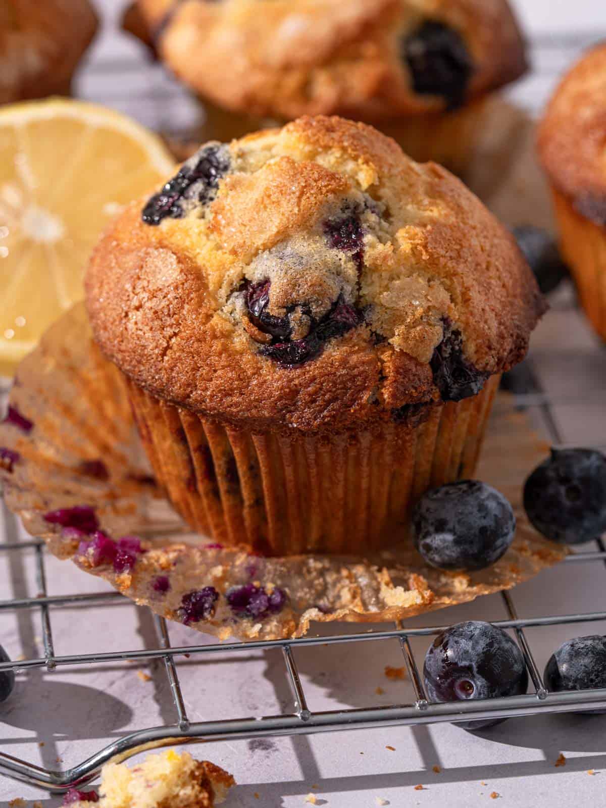 Muffins on a rack with crumbs and blueberries around.