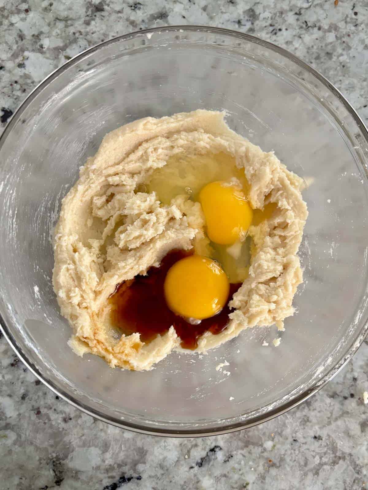 Egg, egg yolk, vanilla, and almond extract being added to the butter sugar mixture.