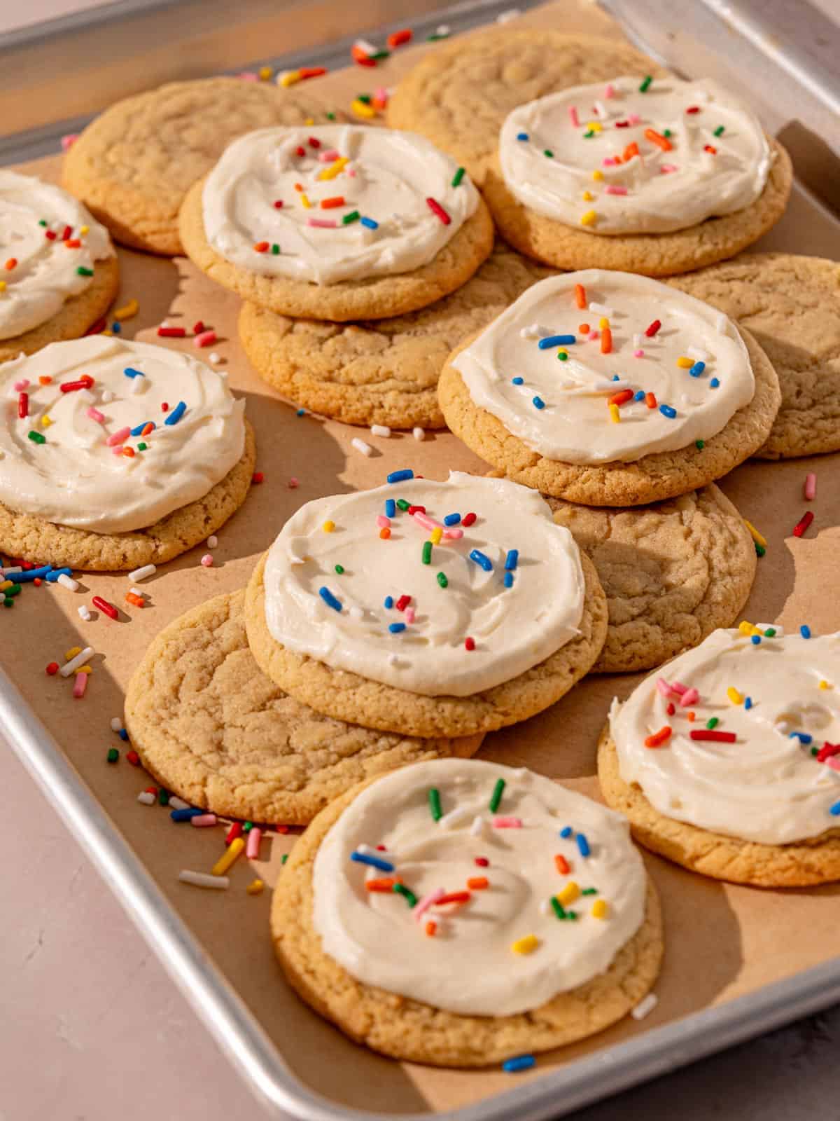 Baked sugar cookies with frosting on a baking sheet.