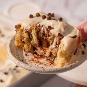 A bite taken out of a chocolate cinnamon roll with icing on top.