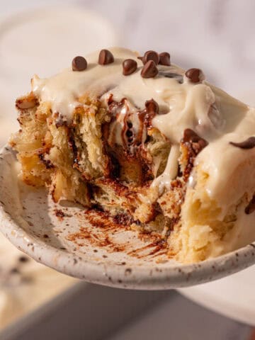 A bite taken out of a chocolate cinnamon roll with icing on top.