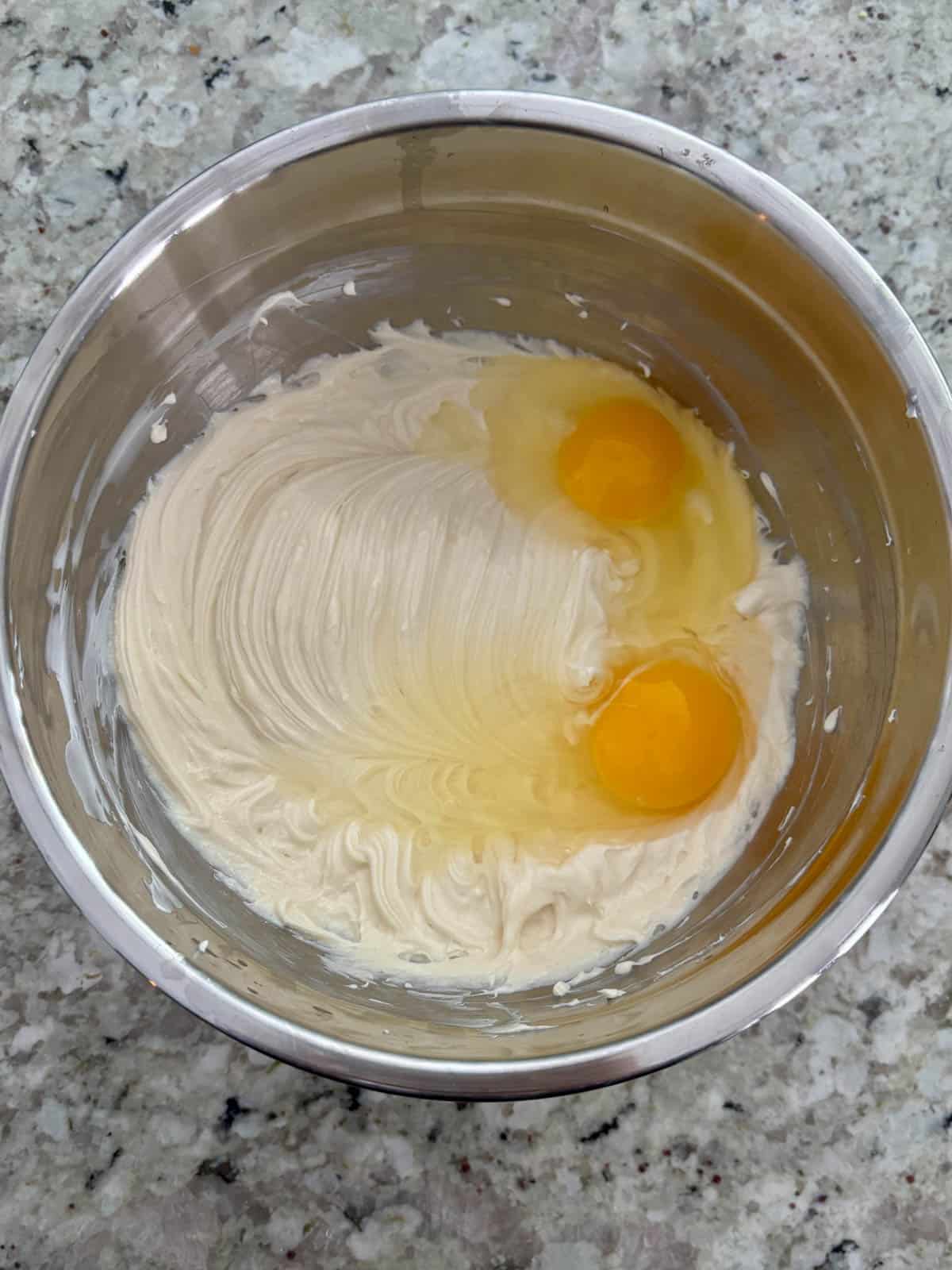 Eggs being added to the cream cheese mixture in a bowl.