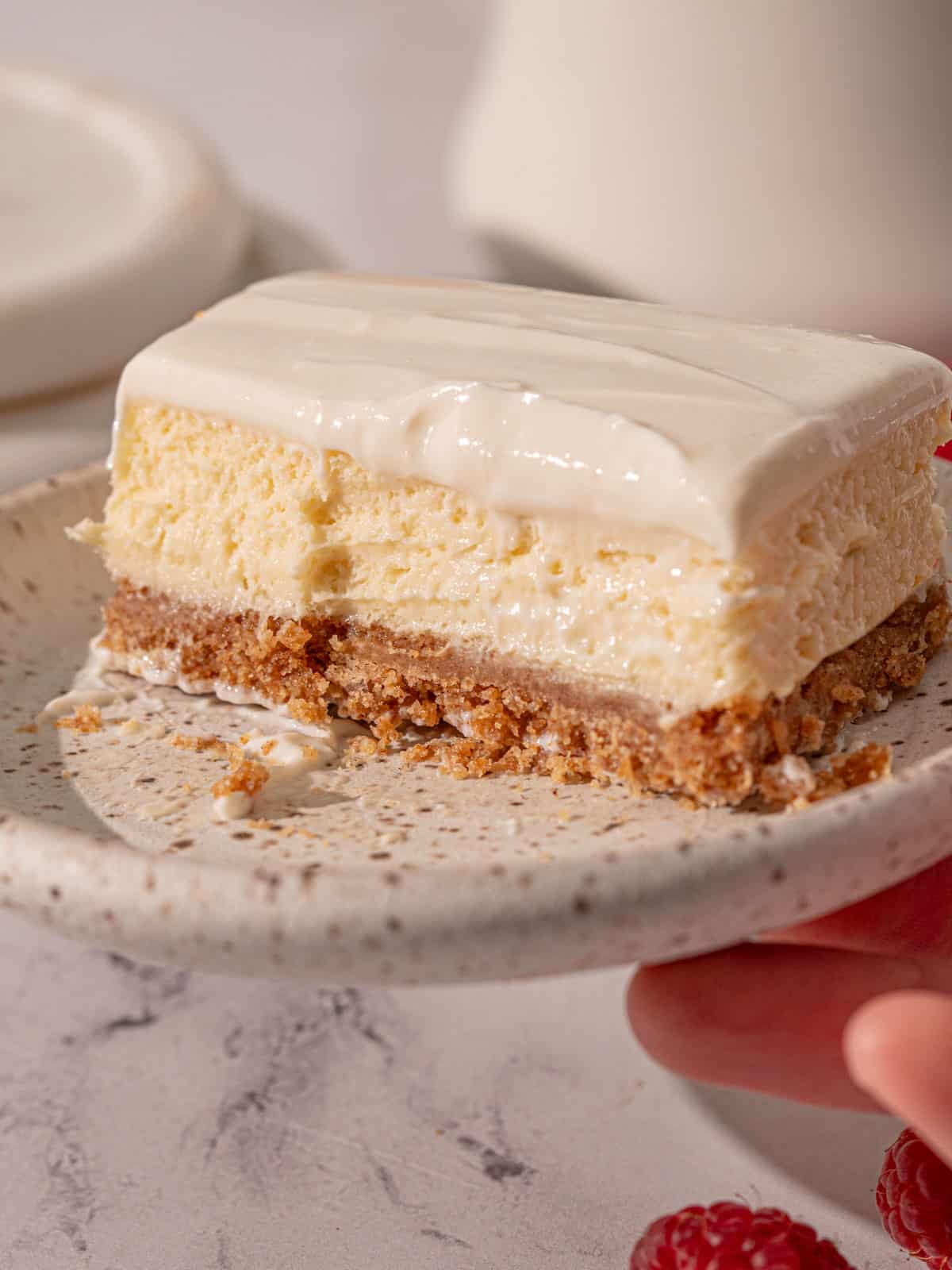 Vanilla cheesecake with sour cream topping on a plate with a bite taken out of it.