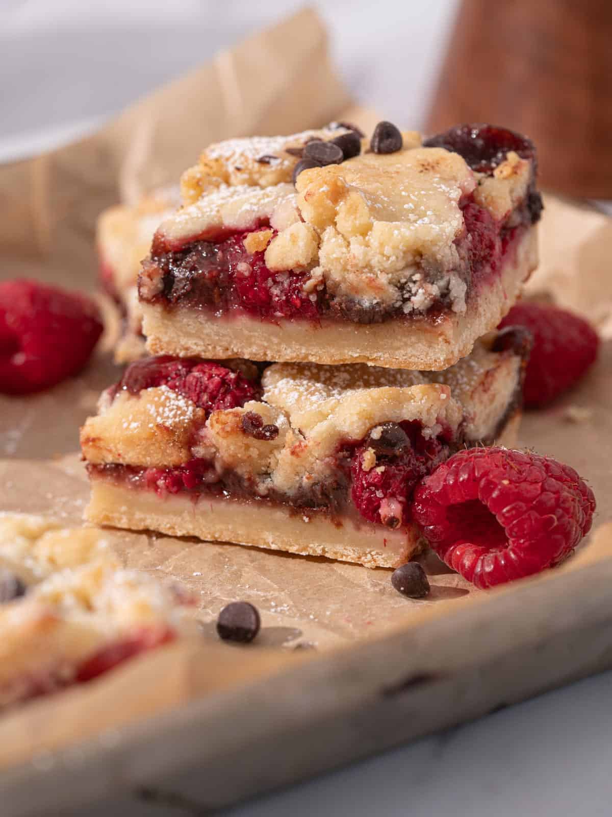 Raspberry bars with chocolate chips and fresh raspberries stacked.