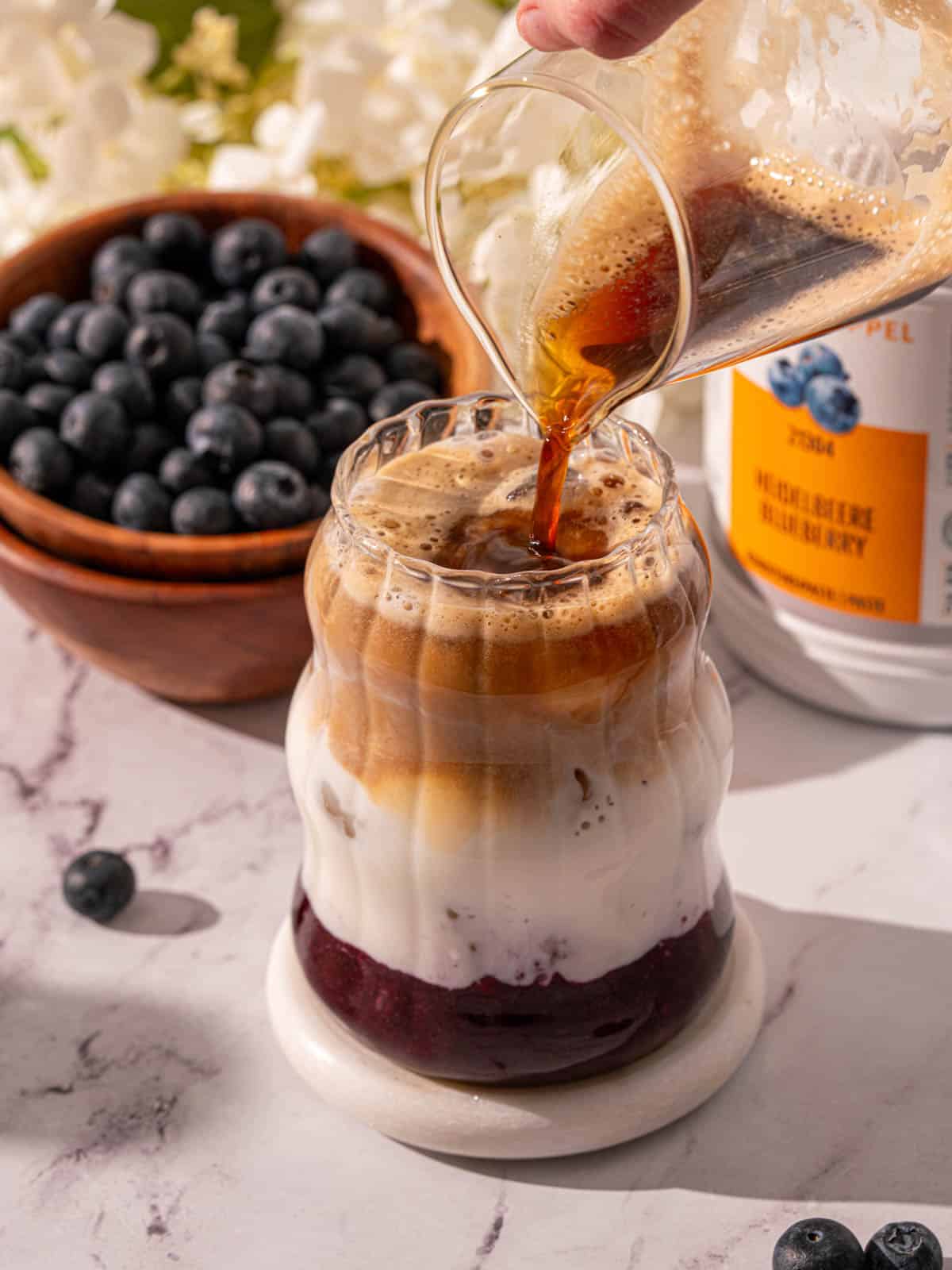 Adding espresso to a glass with milk and blueberry syrup.