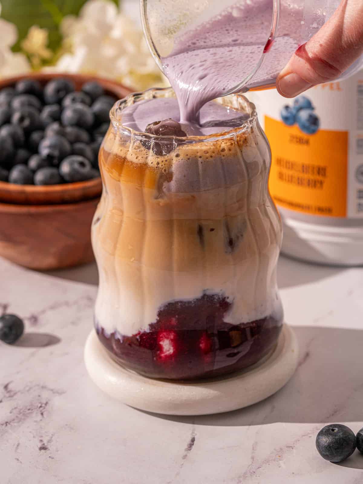 Blueberry cold foam being poured on top of the latte.