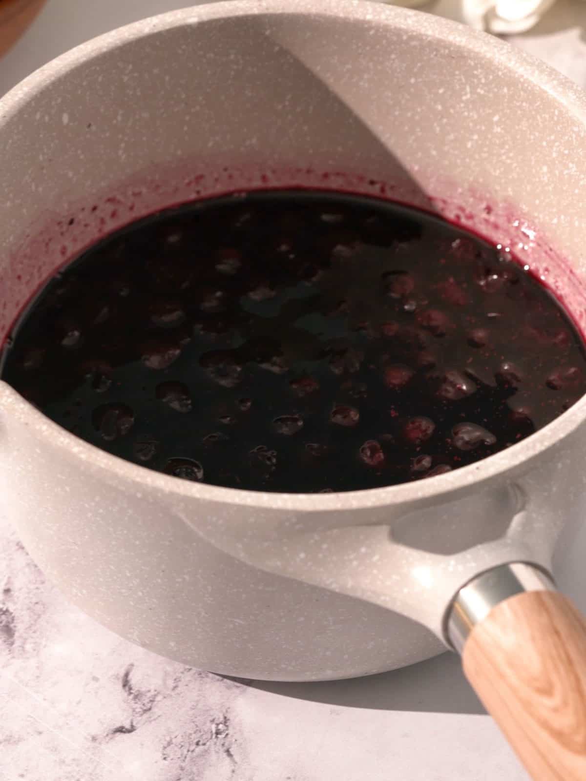 Blueberries, sugar, and cinnamon being cooked down in a saucepan.