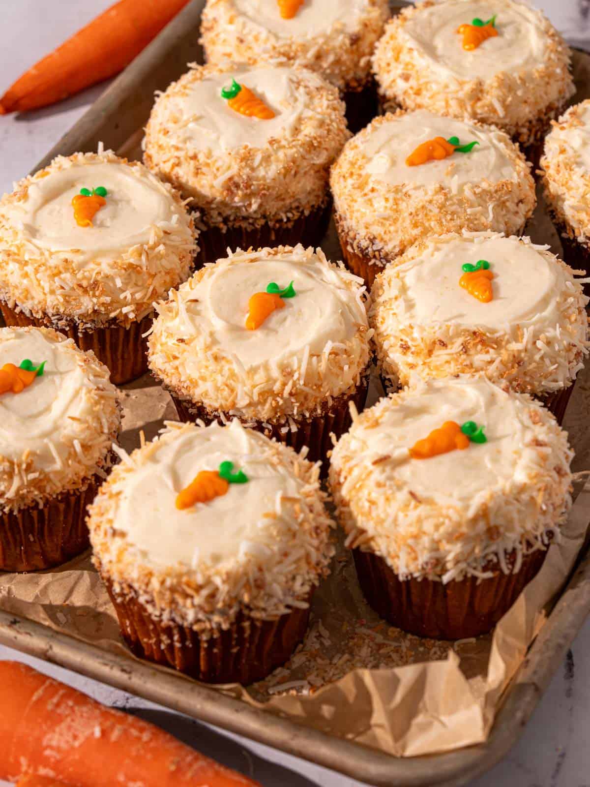 Carrot cupcakes with mini carrots on top and toasted coconut around the edges.