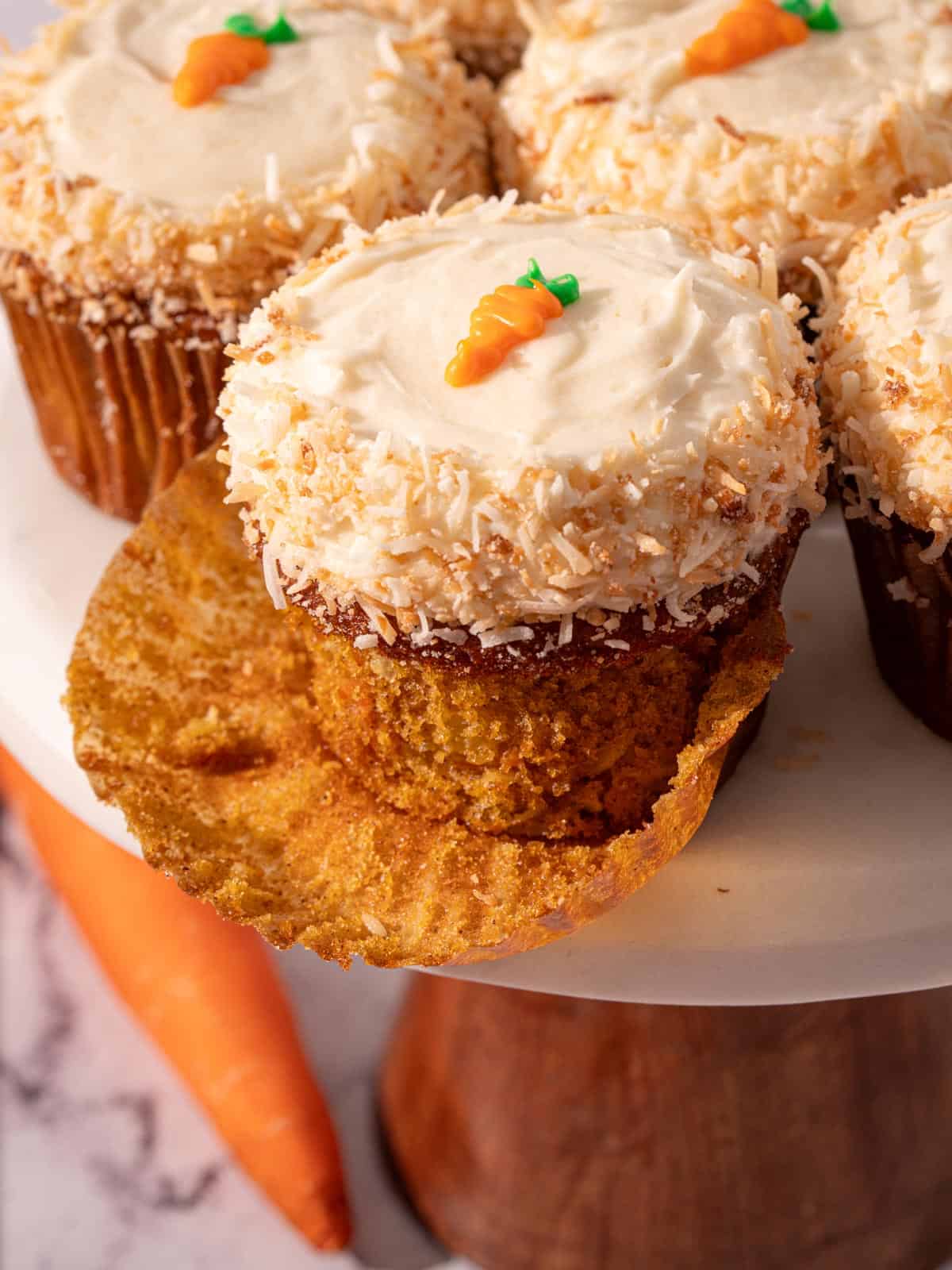 Carrot and pineapple cake with coconut on a cake stand with a carrot around it.