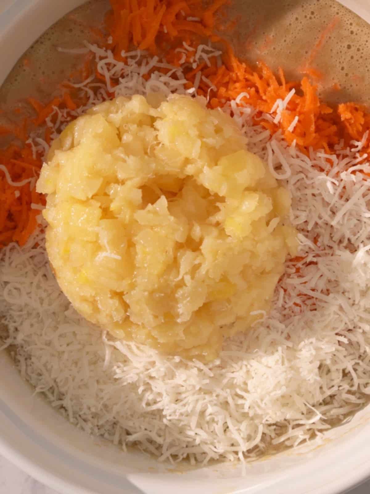 Shredded carrots, crushed pineapple, and coconut being added to the bowl.