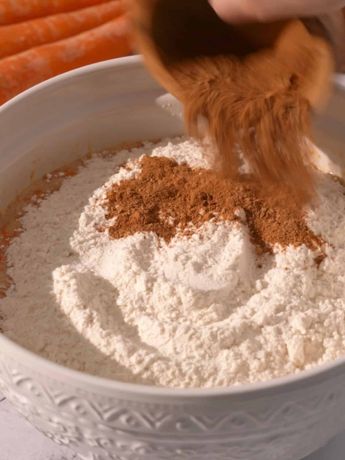 The flour, baking soda, baking powder, salt, and spices being added to the wet ingredients in a bowl.