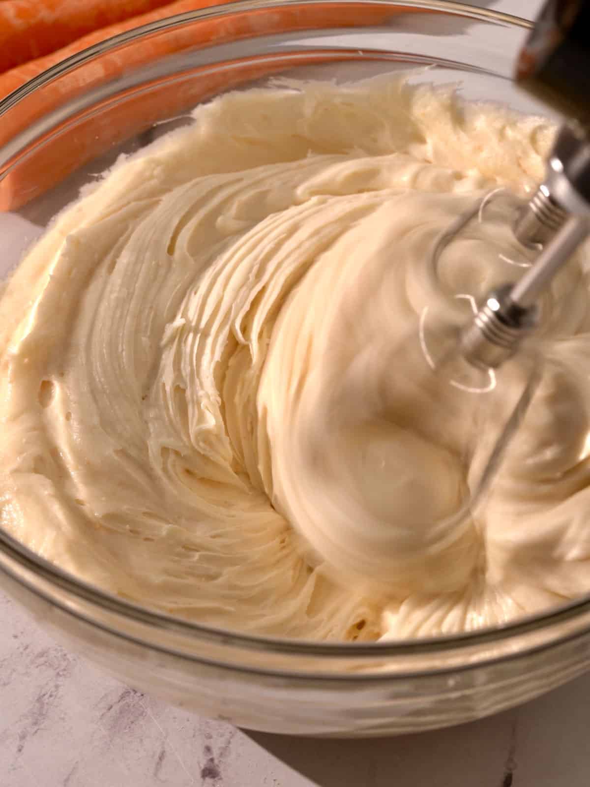 Cream cheese frosting in a bowl being mixed until smooth.