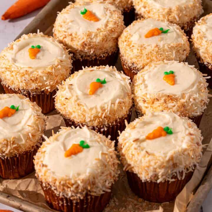 Carrot cake with coconut around the edges and mini carrots on top on a piece of parchment paper.