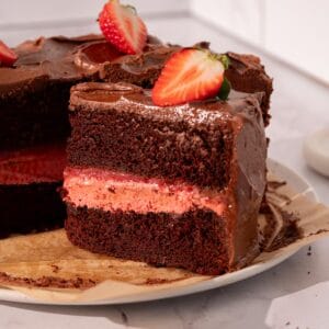 Strawberry filled chocolate cake on a plate with fresh strawberries and parchment paper.
