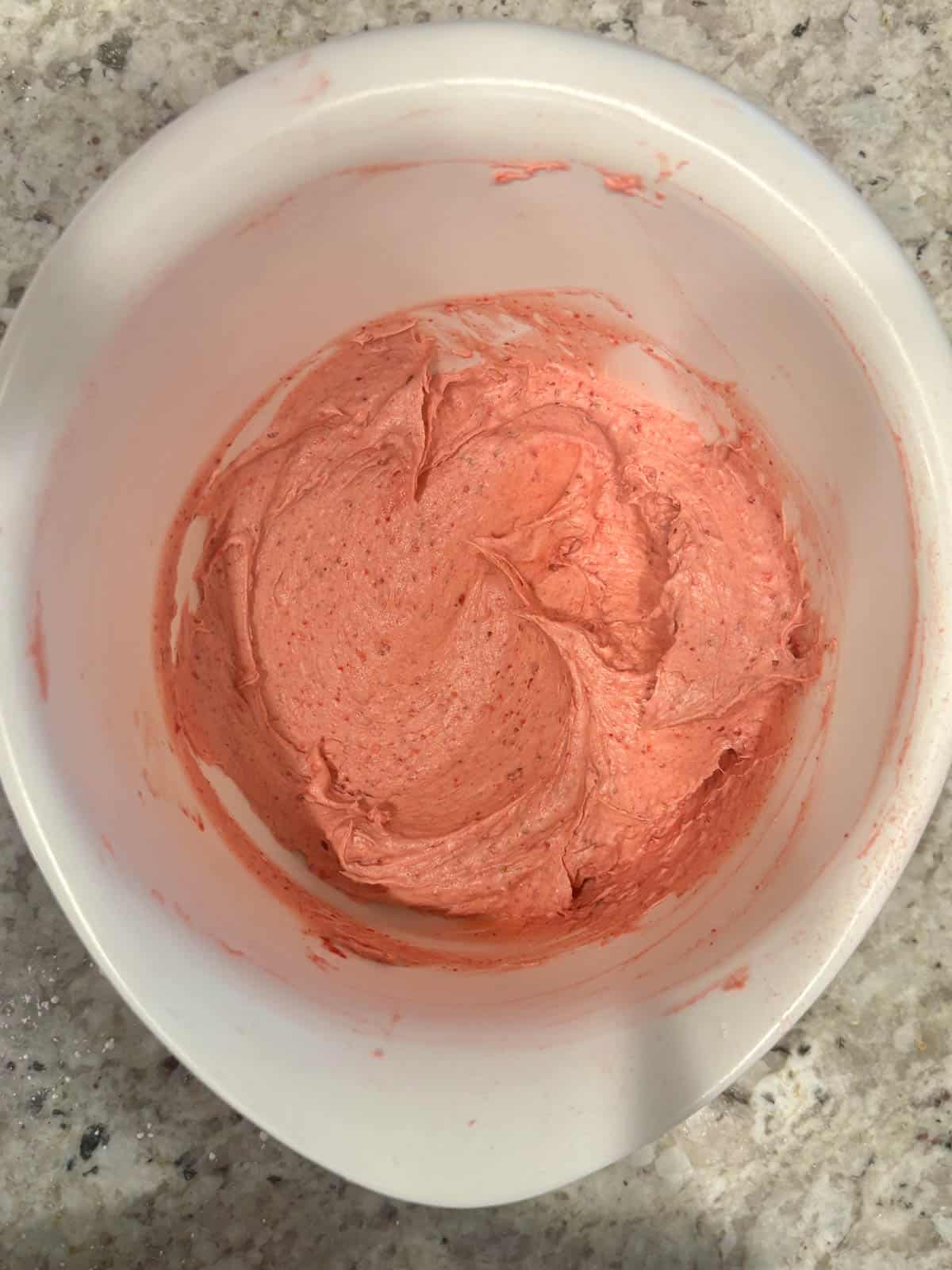 Strawberry frosting filling in a white bowl on the counter.