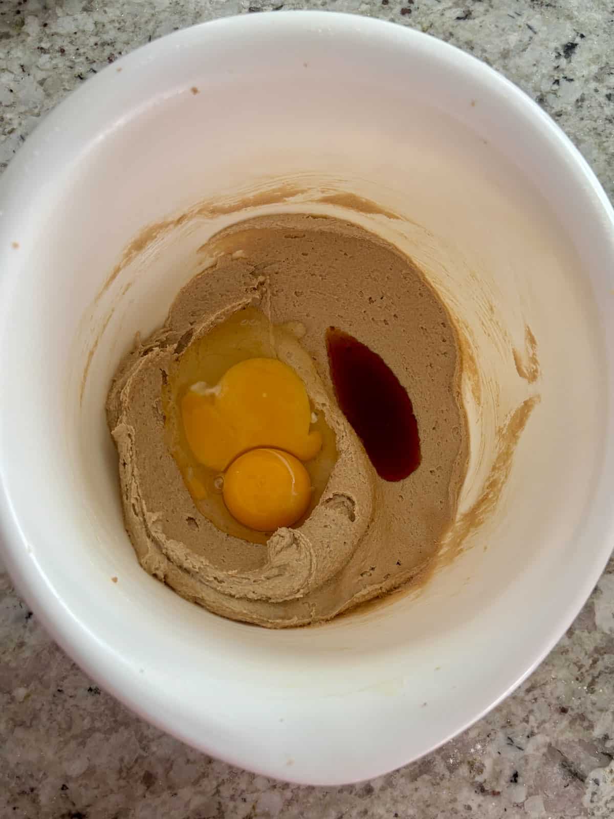 Egg, egg yolk, and vanilla extract being added to the butter sugar mixture in a bowl.
