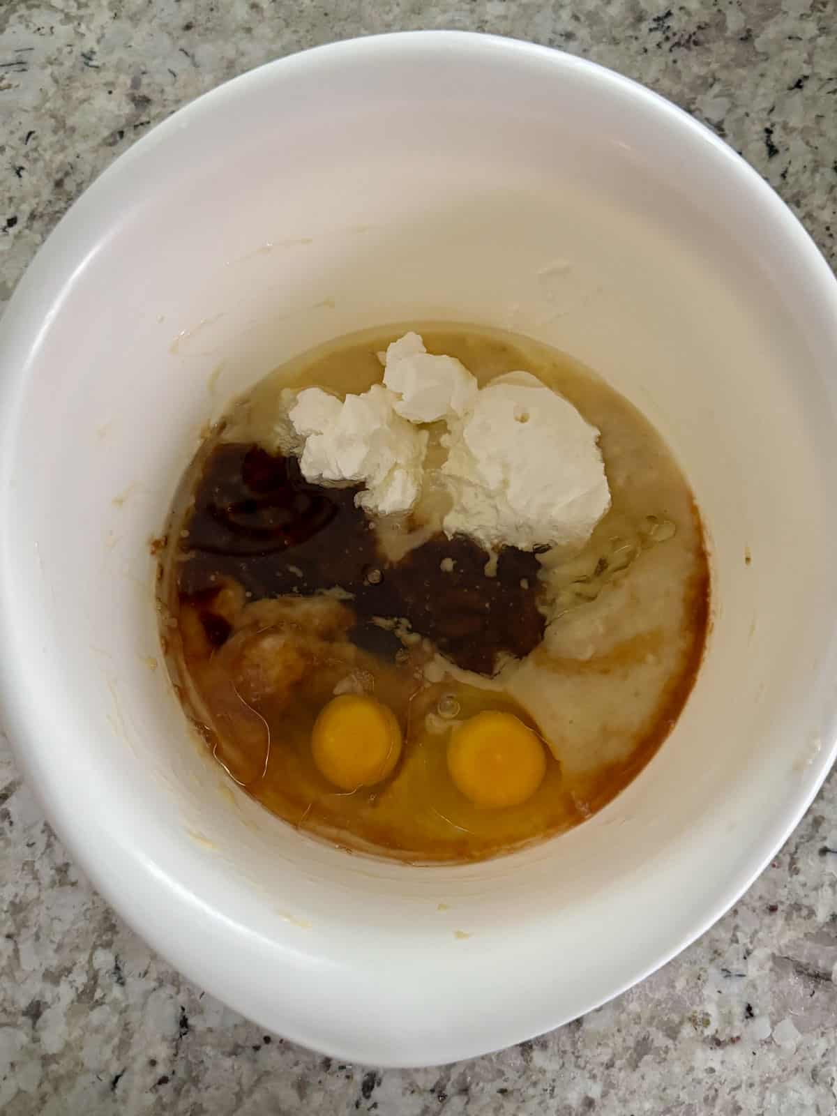 Mashed banana, eggs, sour cream, oil, and brown sugar being mixed together in a bowl .