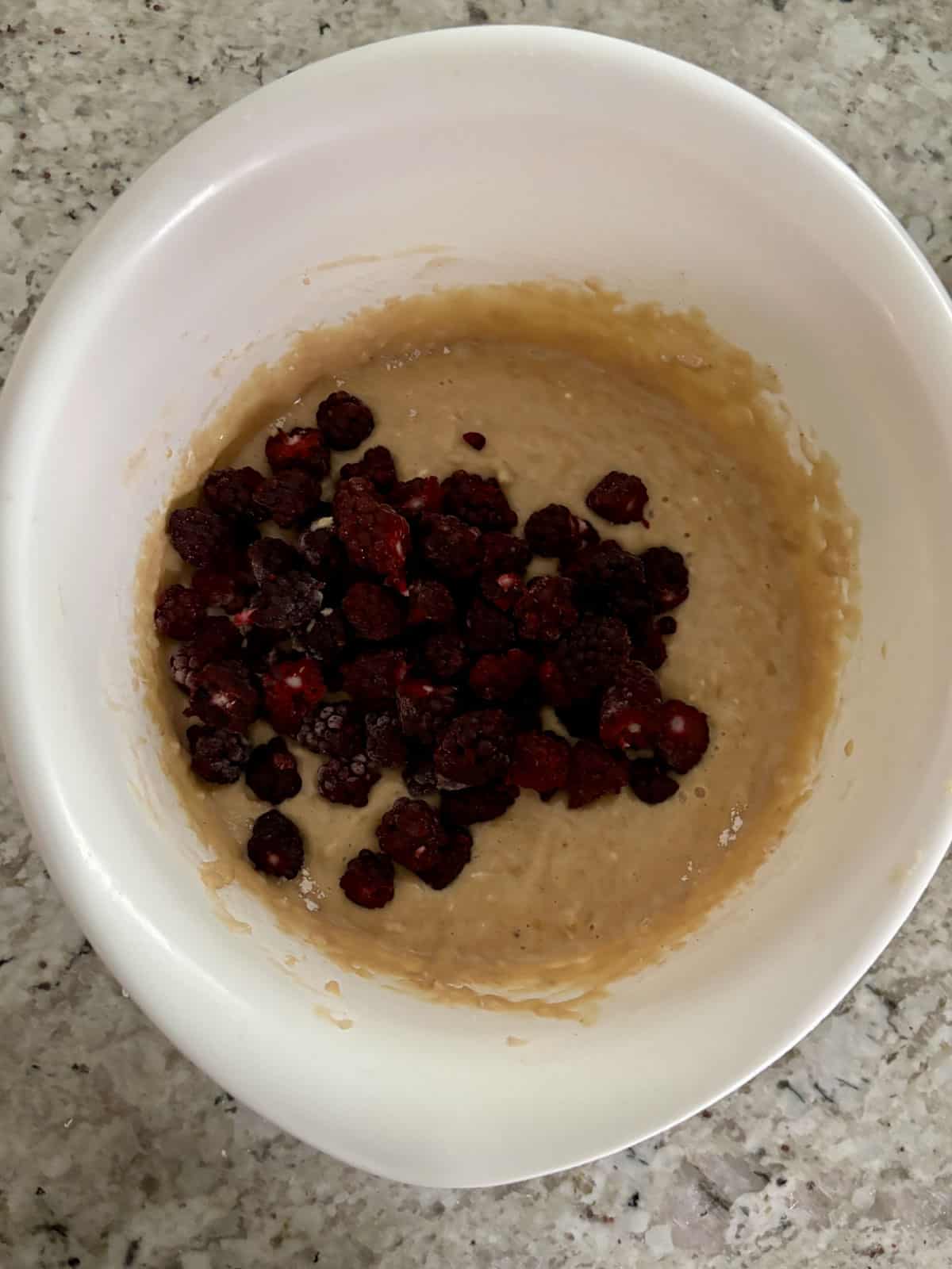 Blackberries being added to the banana muffin batter in a bowl.