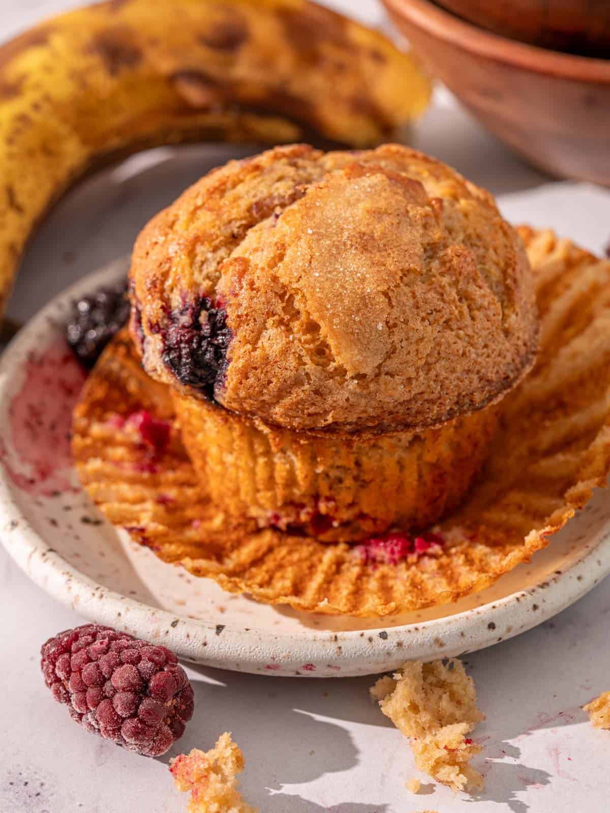 A banana muffin with blackberries on a plate with blackberries around it.
